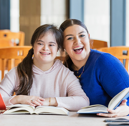 Duas jovens sorrindo com livros, contexto de educação especial e inclusiva